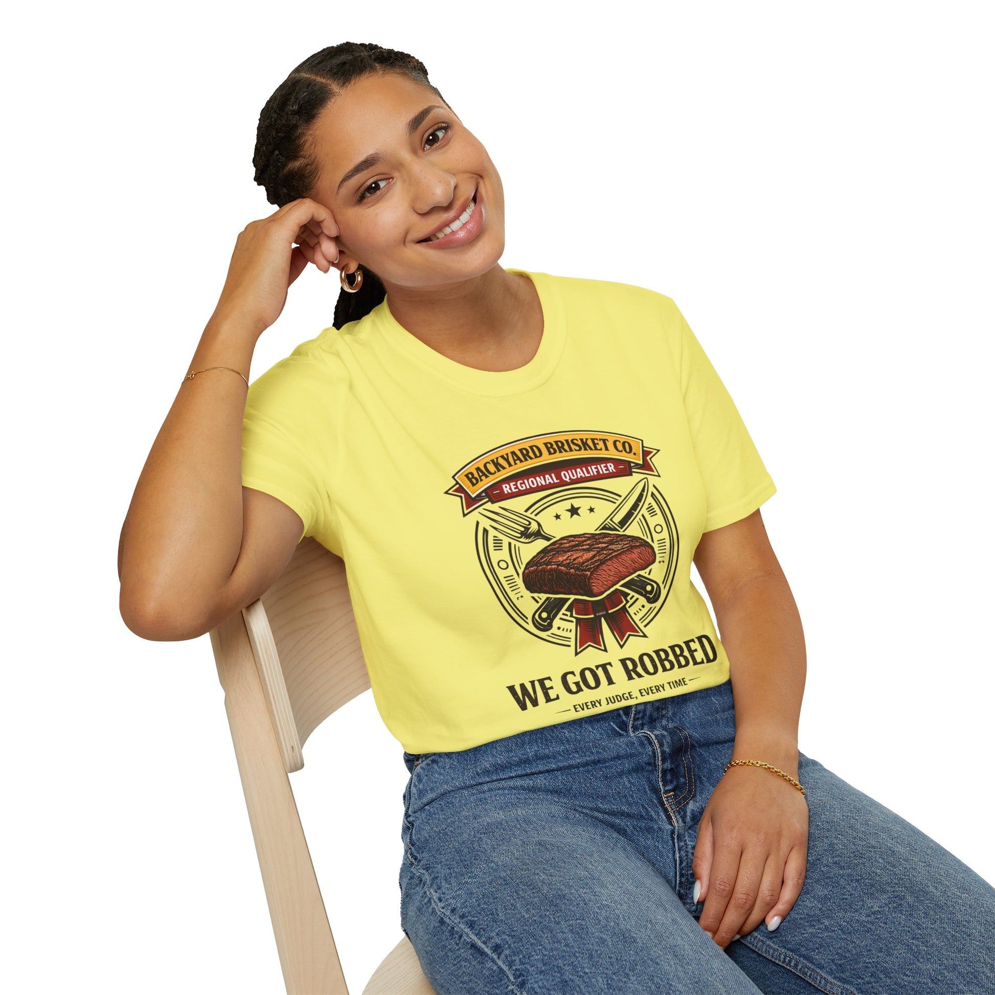 Backyard Brisket Co. Shirt, Cornsilk pale yellow, worn by a model seated on a wooden chair