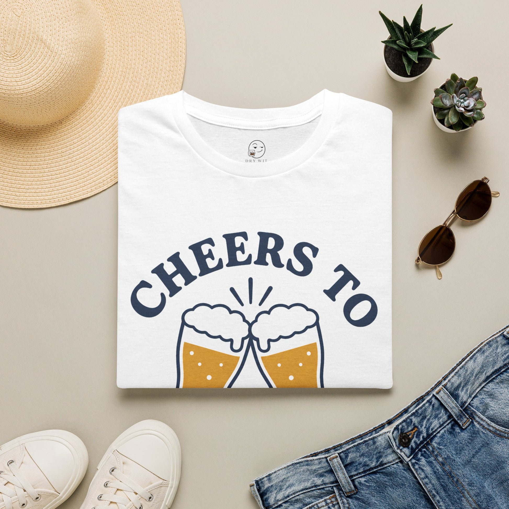 Cheers to Lowering Expectations Shirt, White, folded flat lay styled with a straw hat, sunglasses, sneakers and denim