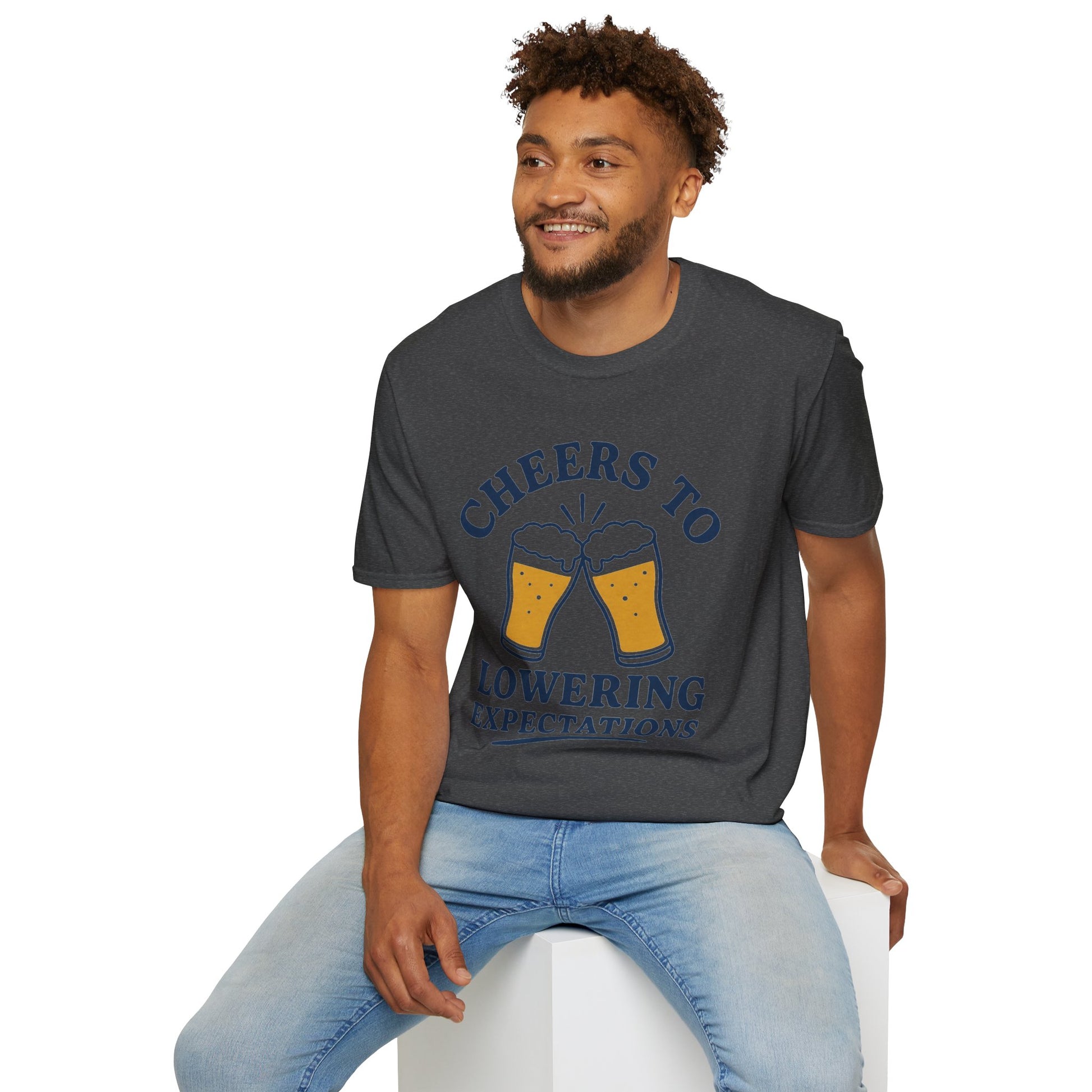Cheers to Lowering Expectations Shirt, Dark Heather charcoal, worn by a model seated on a white block