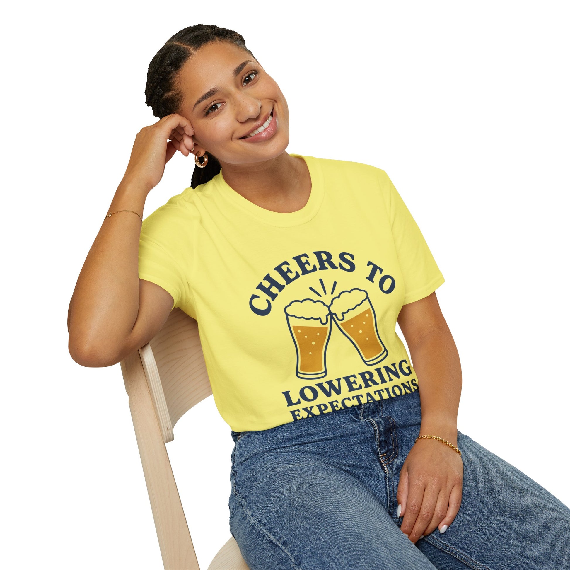Cheers to Lowering Expectations Shirt, Cornsilk pale yellow, worn by a model seated on a wooden chair