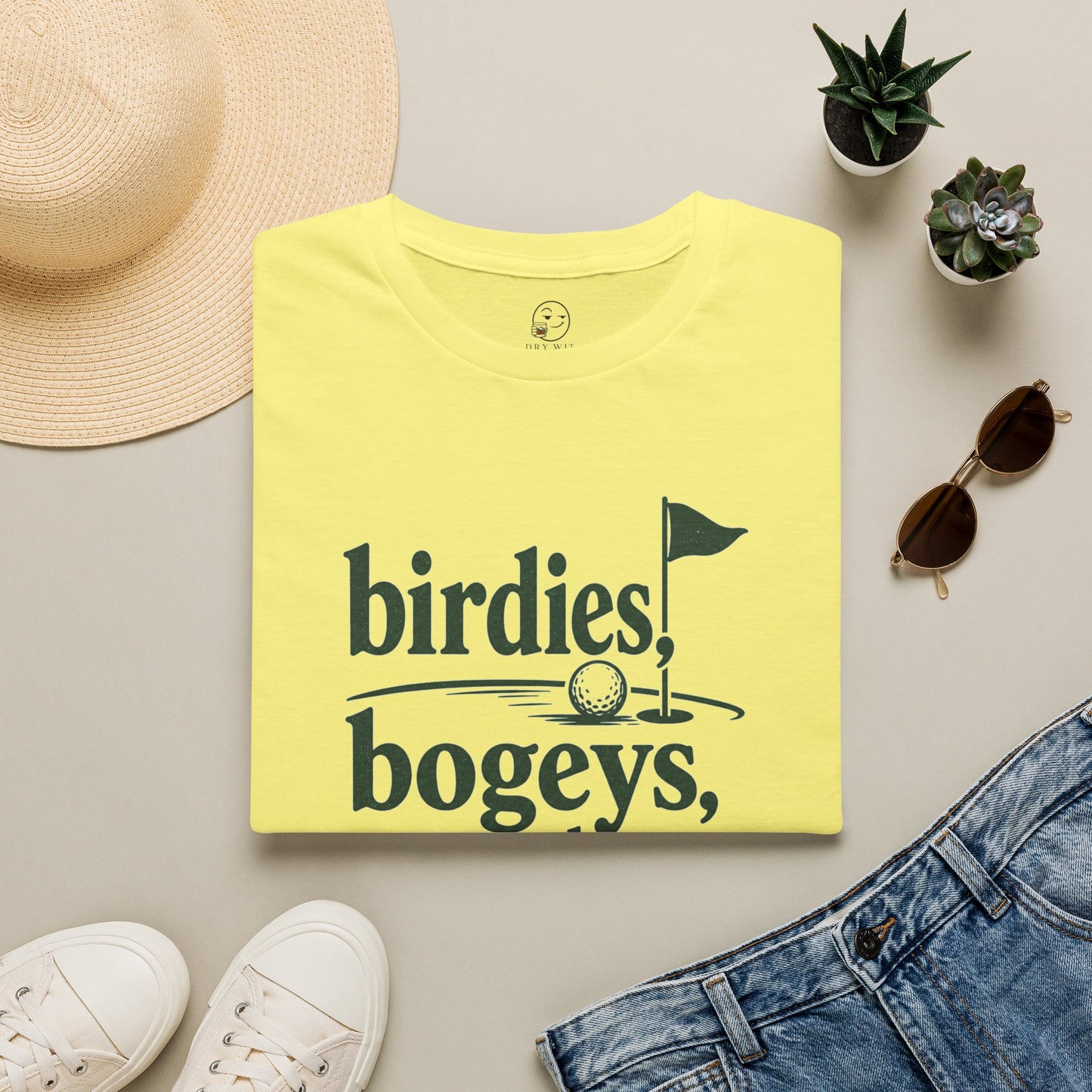 Birdies, Bogeys, and Bourbon Shirt, Cornsilk pale yellow, folded flat lay styled with a straw hat, sunglasses, sneakers and denim