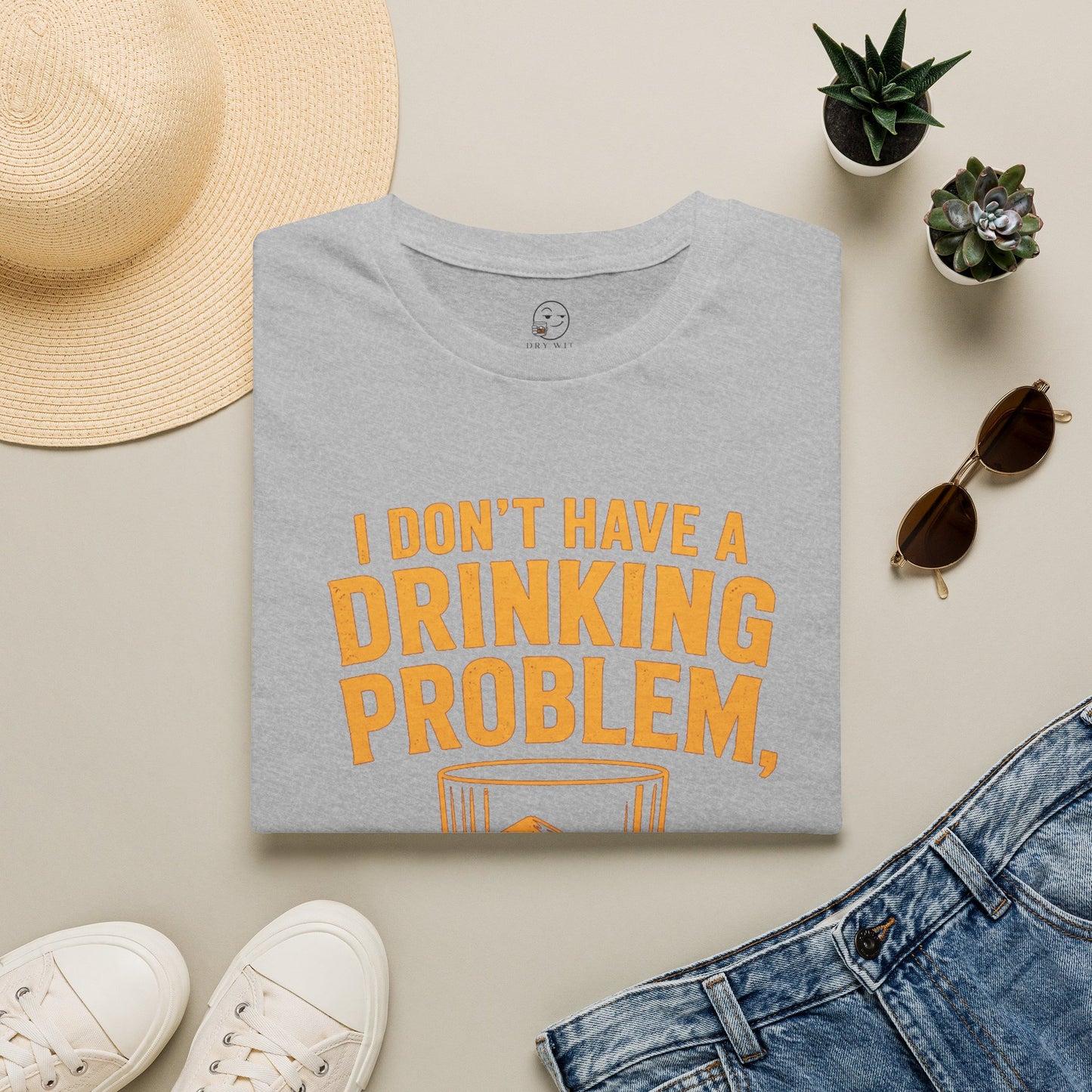 I Don't Have a Drinking Problem Shirt, Sport Grey, folded flat lay styled with a straw hat, sunglasses, sneakers and denim