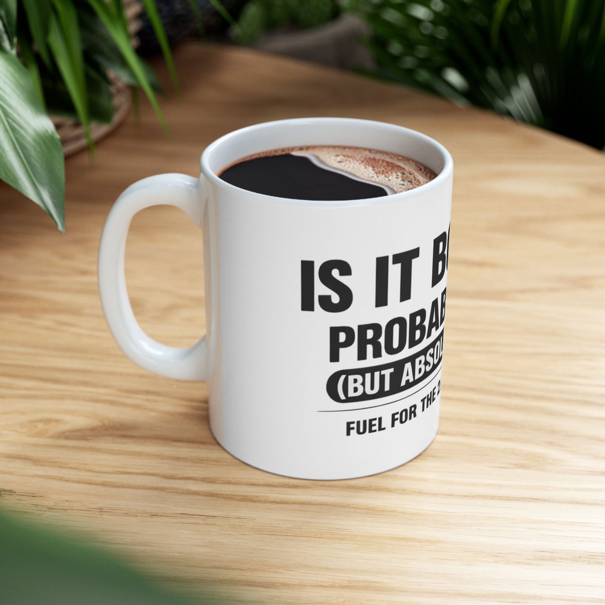 Is It Booze Mug, white ceramic, lifestyle shot on a wooden table beside houseplants, filled with black coffee, handle on the left