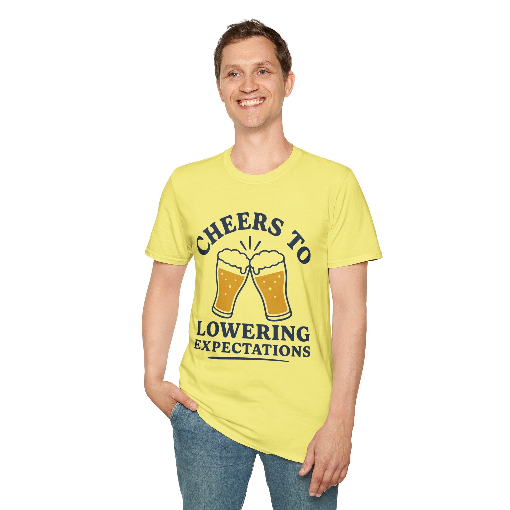 Cheers to Lowering Expectations Shirt, Cornsilk pale yellow, worn by a standing model with one hand in their pocket