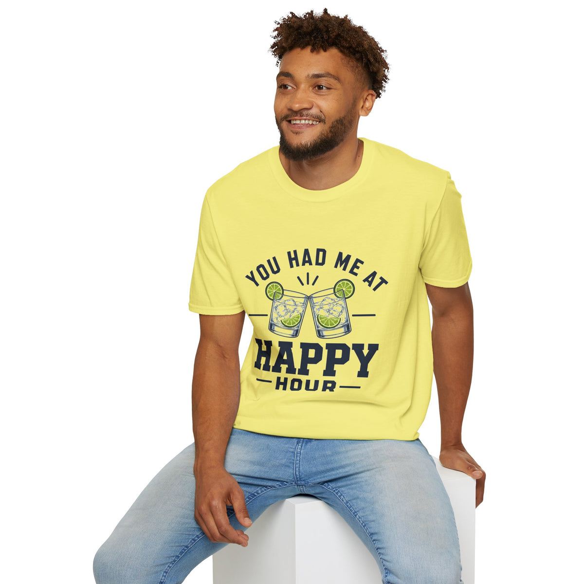 You Had Me At Happy Hour Shirt, Cornsilk pale yellow, worn by a model seated on a white block