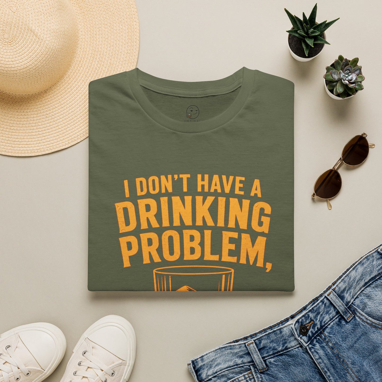 I Don't Have a Drinking Problem Shirt, Military Green olive, folded flat lay styled with a straw hat, sunglasses, sneakers and denim