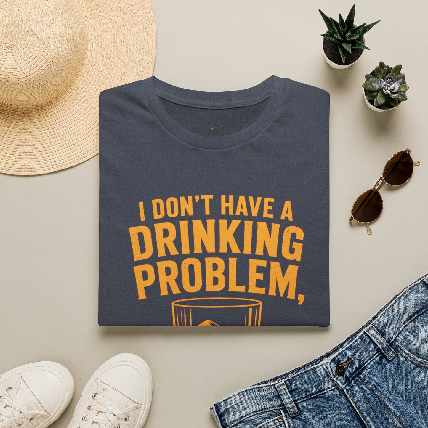 I Don't Have a Drinking Problem Shirt, Heather Navy, folded flat lay styled with a straw hat, sunglasses, sneakers and denim