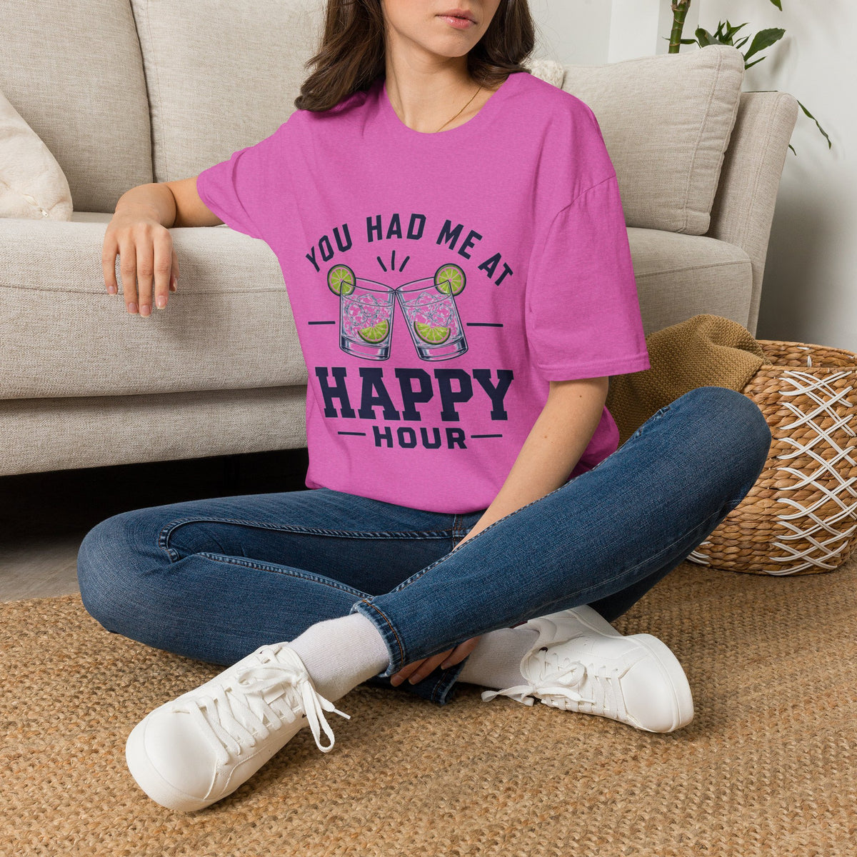 You Had Me At Happy Hour Shirt, Heather Berry pink, worn by a model seated on the floor beside a sofa