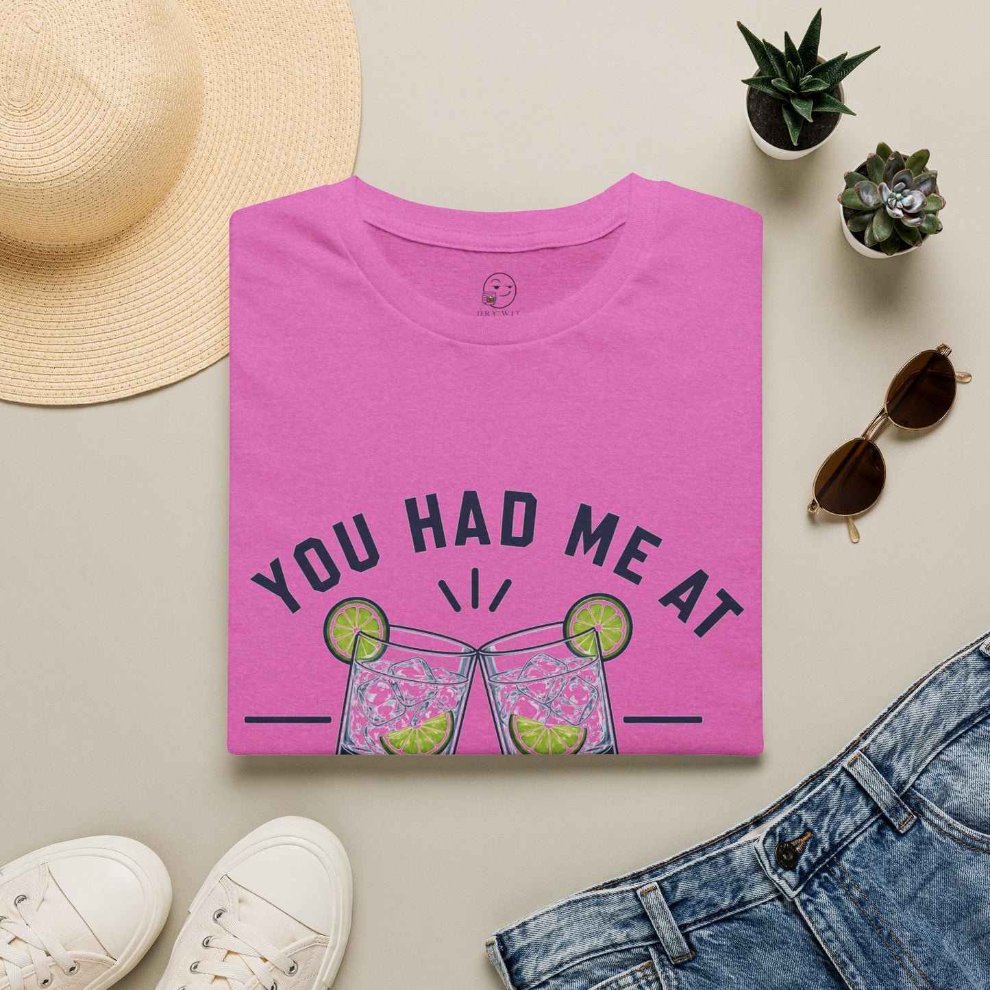 You Had Me At Happy Hour Shirt, Heather Berry pink, folded flat lay styled with a straw hat, sunglasses, sneakers and denim