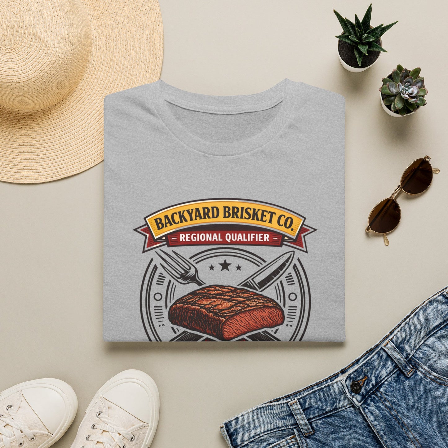 Backyard Brisket Co. Shirt, Sport Grey, folded flat lay styled with a straw hat, sunglasses, sneakers and denim