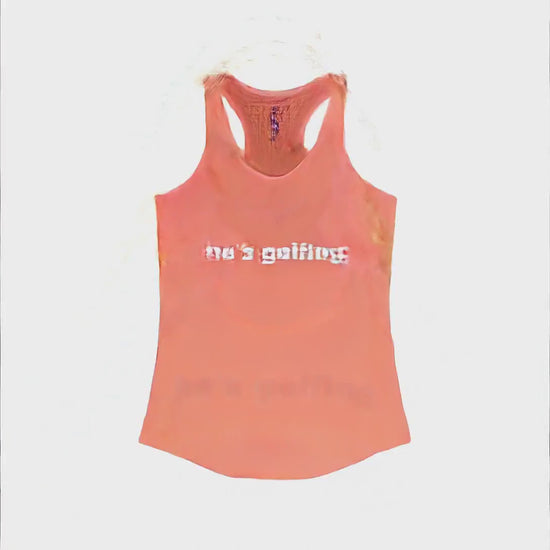 Video of a woman relaxing poolside in a lounge chair holding a drink, giving a playful smirk toward the camera, wearing a coral racerback tank top with white text reading He's Golfing